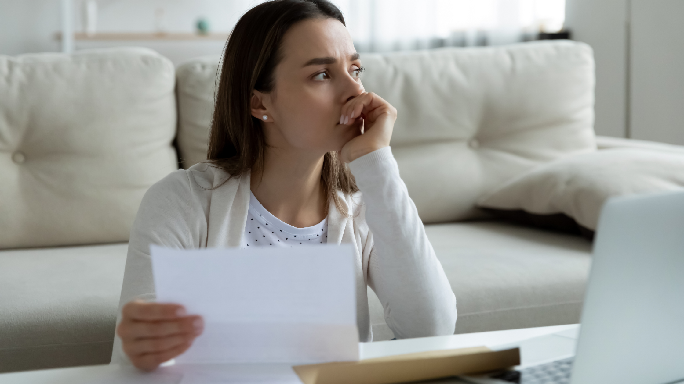 young woman sitting at coffee table with perplexed look reviewing account statement