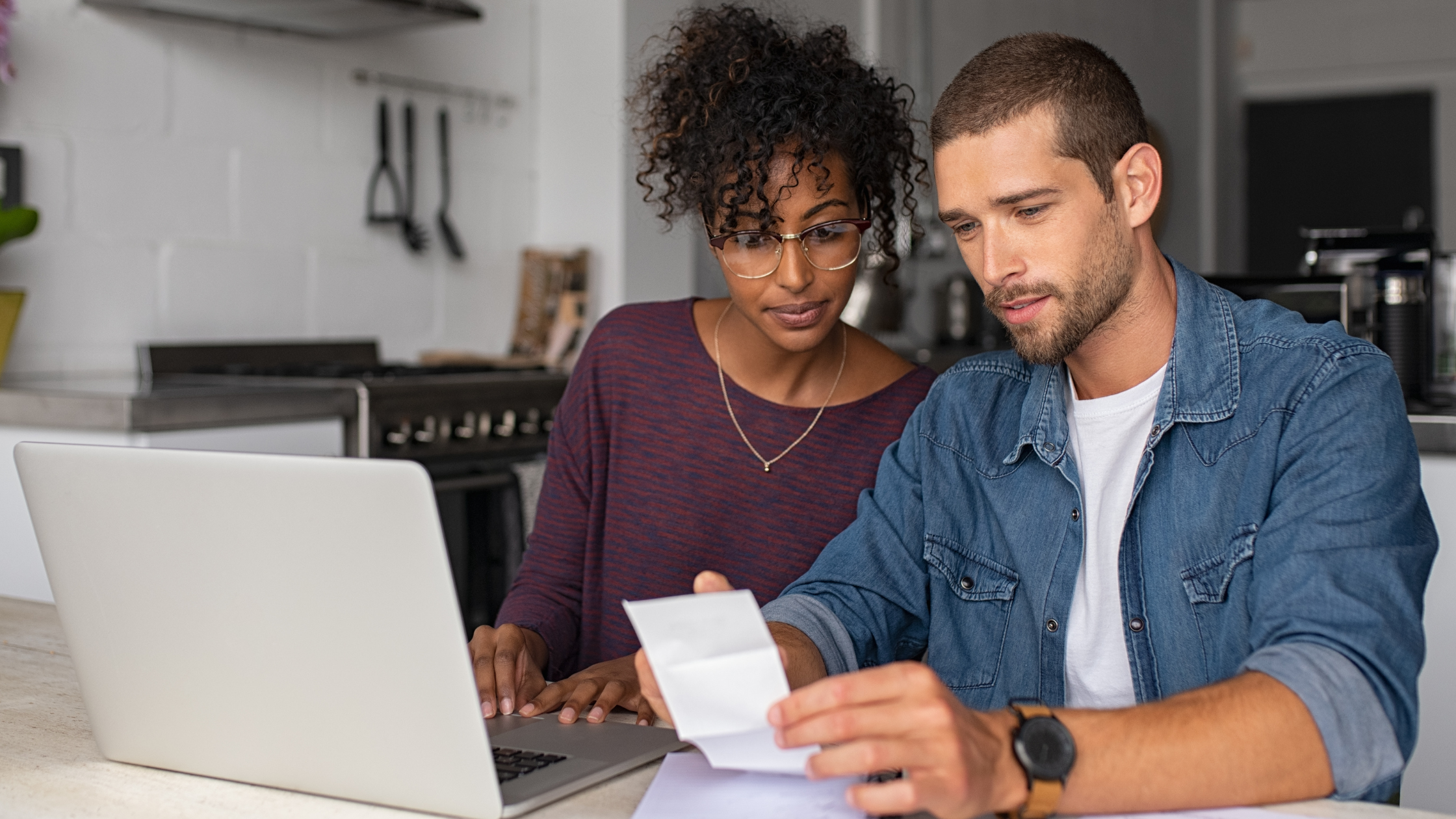 Fall financial checkup blog cover banner - Young couple sitting at table with laptop reviewing budget