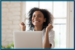 Happy young woman in front of laptop smiling with arms up in excitement