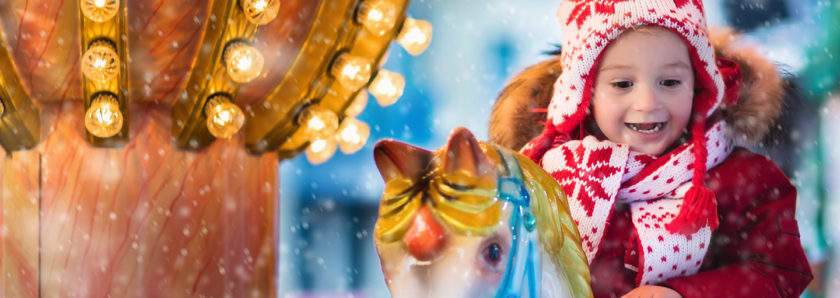 Young girl riding carousel in snow during holiday