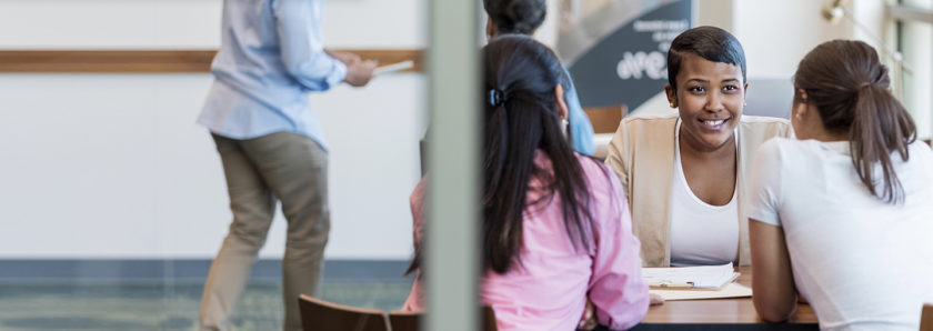 Young african american credit union employee sitting at desk meeting with two female members