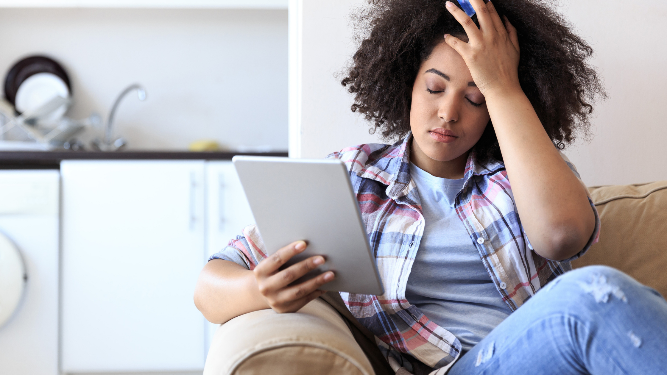 Loan denial blog banner image. Young lady sitting on couch frustrated with hand on head looking at mobile device upon receiving a loan denial notice