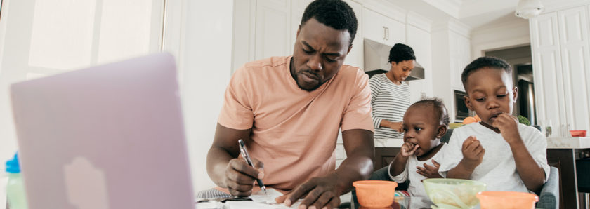 Man at kitchen table with kids and latop looking through papers