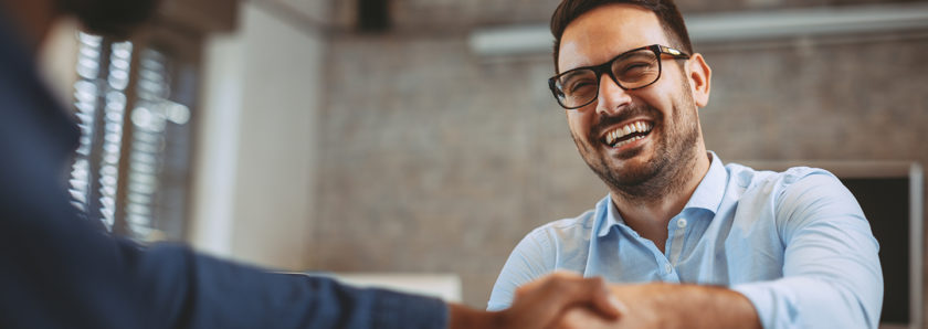 Man with glasses shaking hands across desk