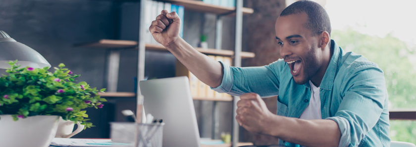 Man throwing hands in the air with excitement while viewing account online at laptop