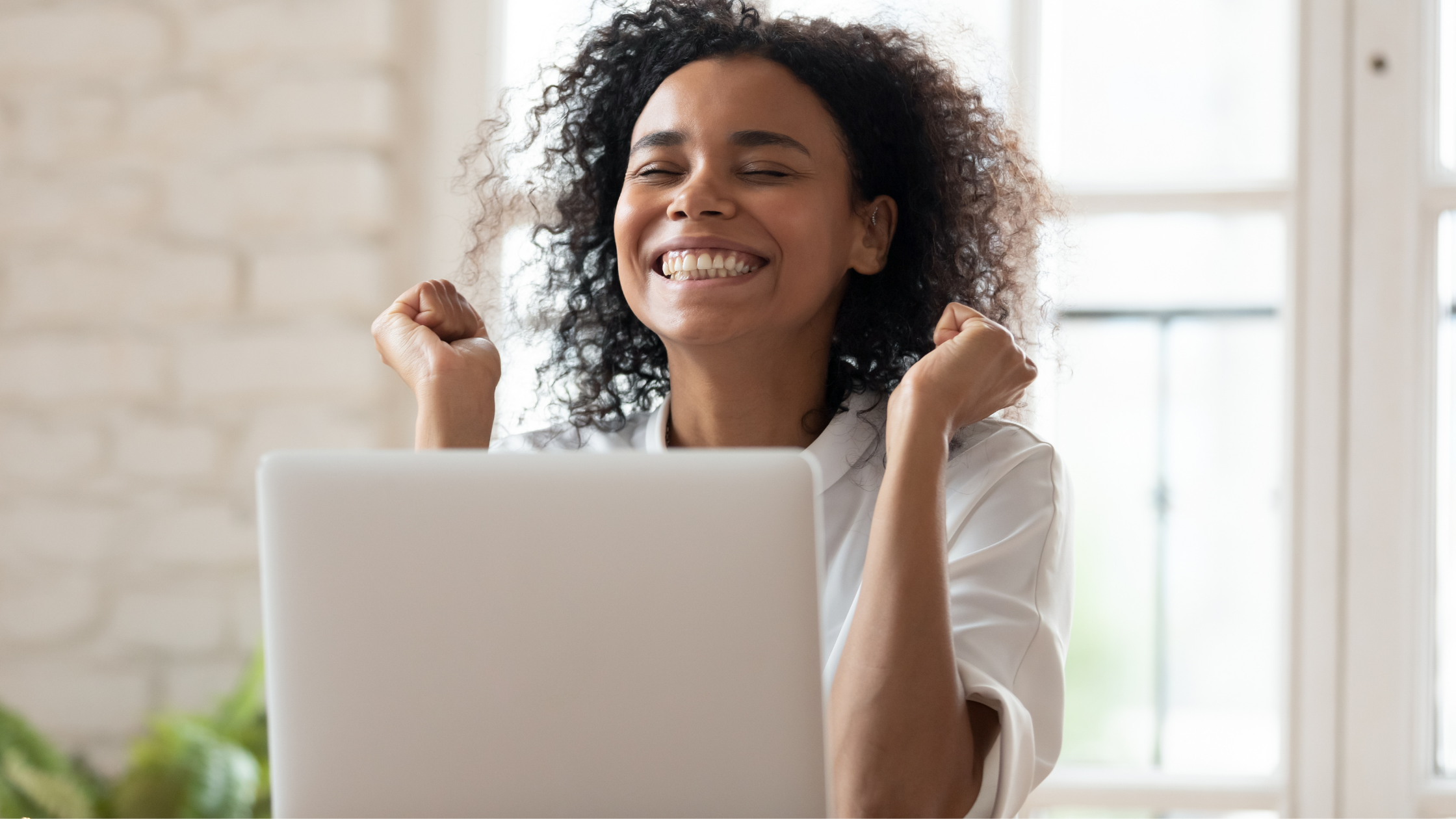 Young women in front of laptop fists up and smiling with excitement