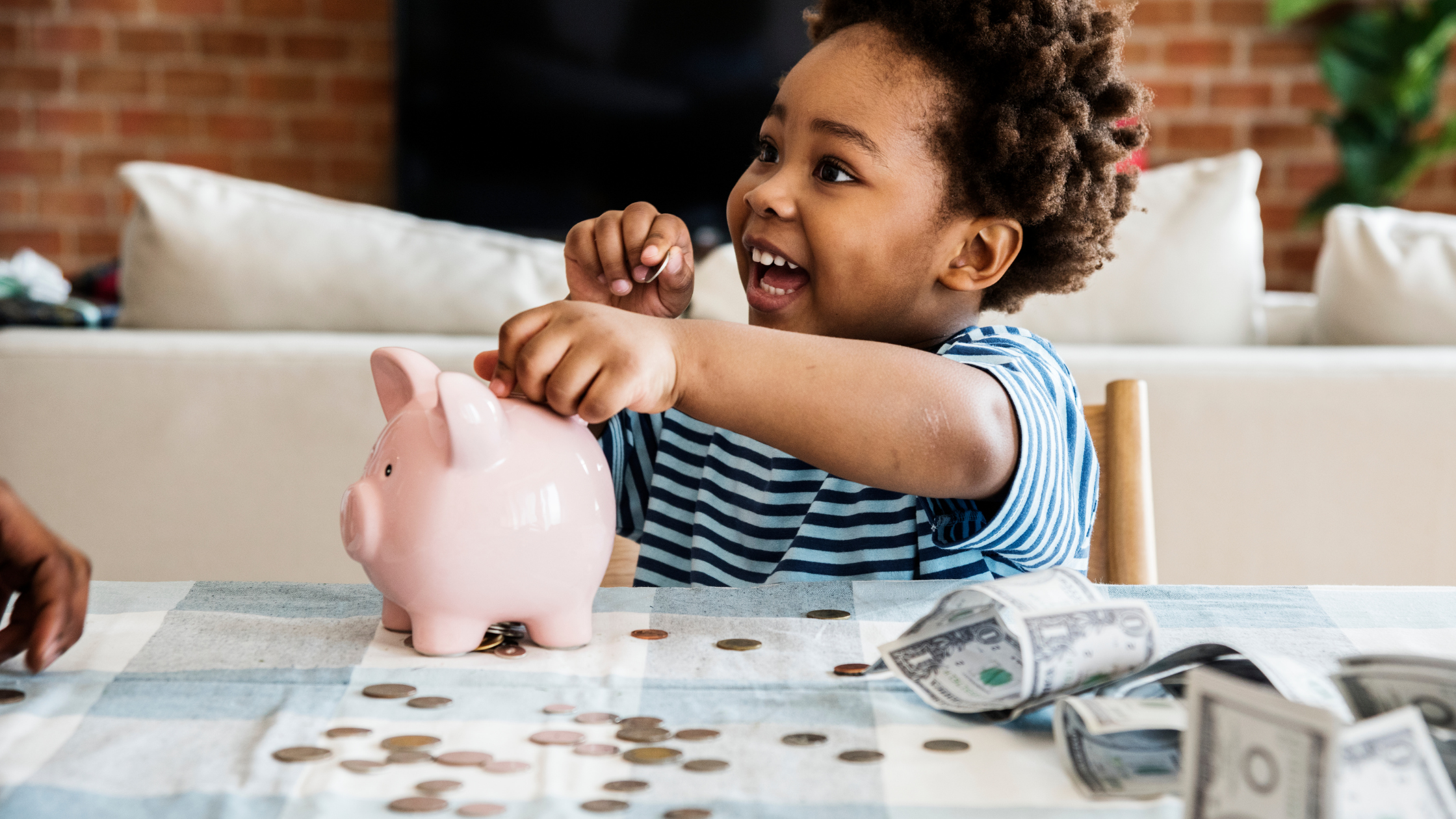 Young boy smiling as he sits at table and adds money into piggy bank. Teaching kids how to save - AFFCU blog