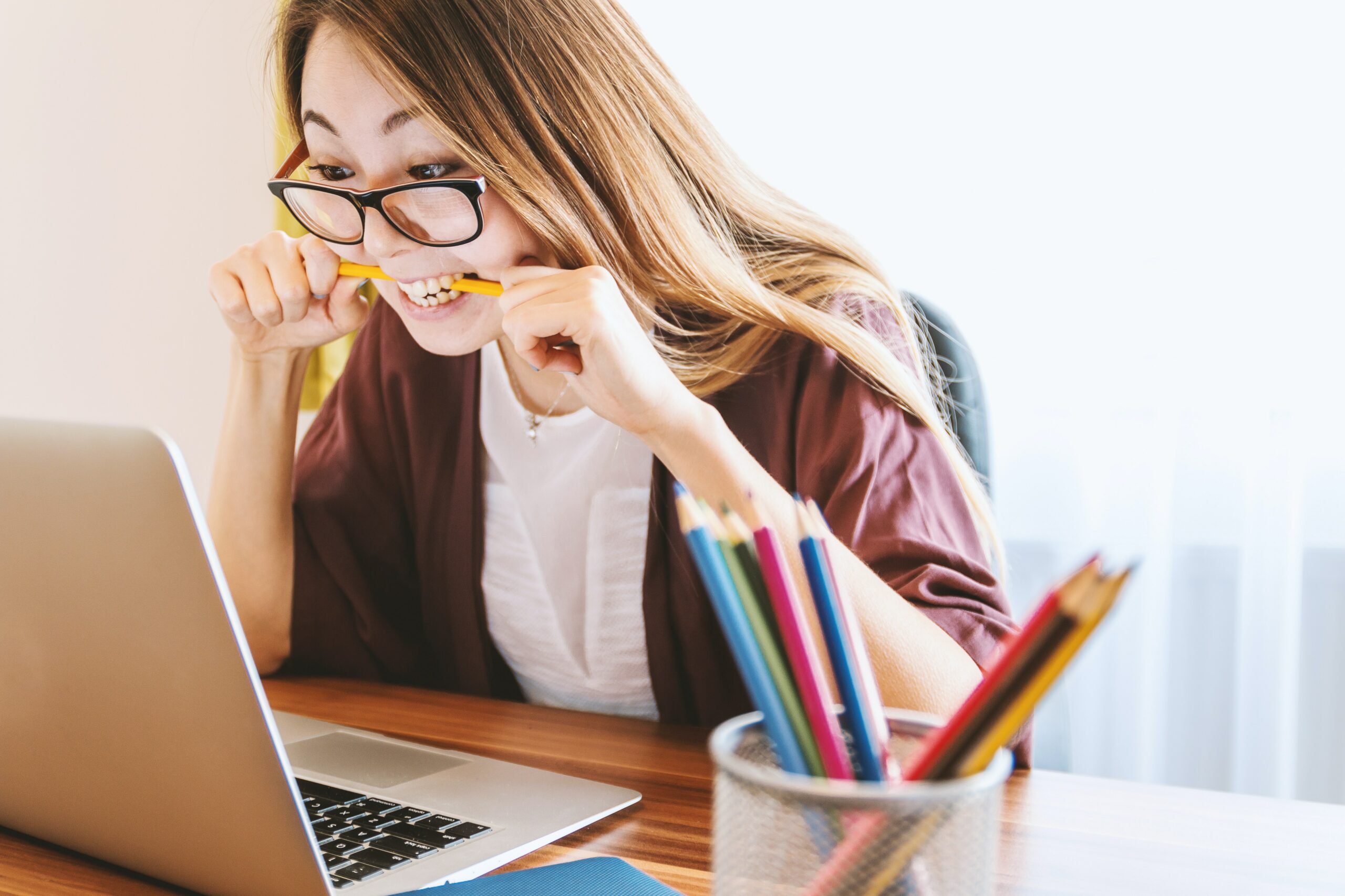 Frustrated young woman biting pencil while looking at account on laptop