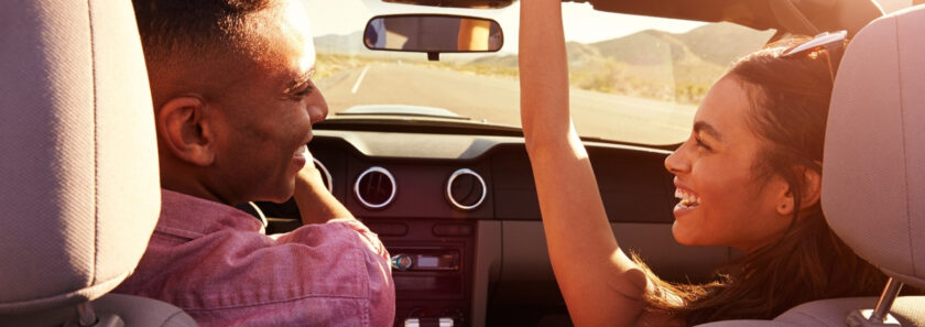 a smiling couple drives with the top down on the convertible car.