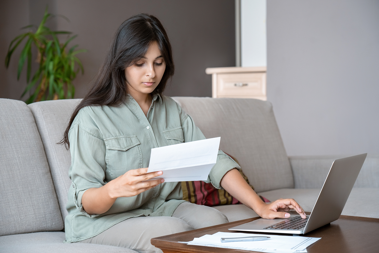 a young woman looks over a bill while she balances her checkbook online