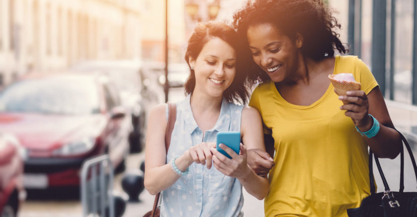 Two young ladies walking down street looking at mobile phone