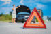 Road hazard triangle on street with car in background with hood open