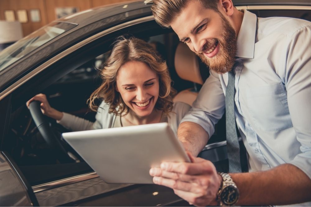 a woman works with a salesman at the dealership on a deal to trade in her car that's not paid off